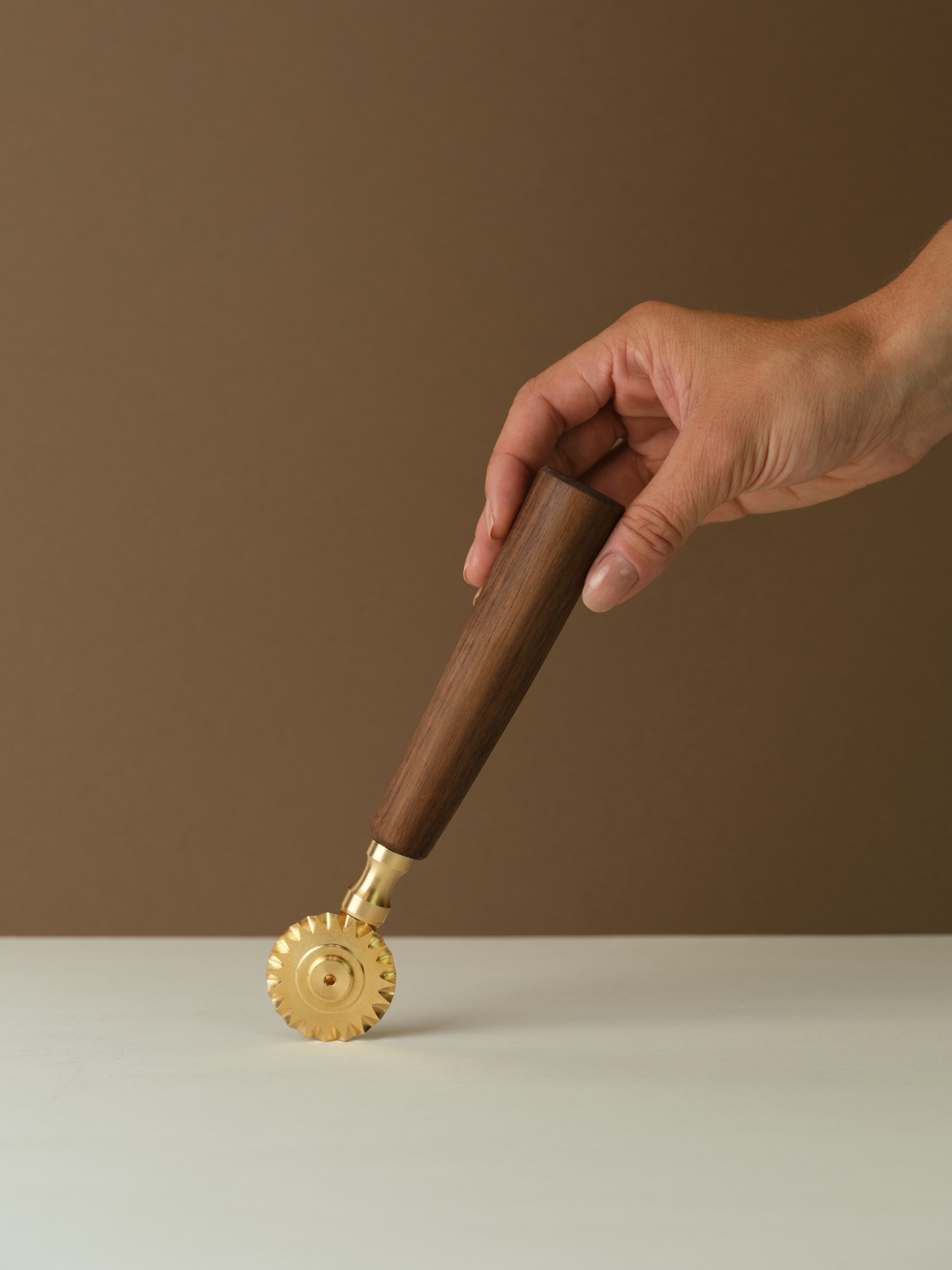 Katto ravioli cutter with brass wheel and walnut wood handle, held at an angle